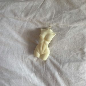 An artistic sculptural candle shaped like a human torso laying on a white sheet.