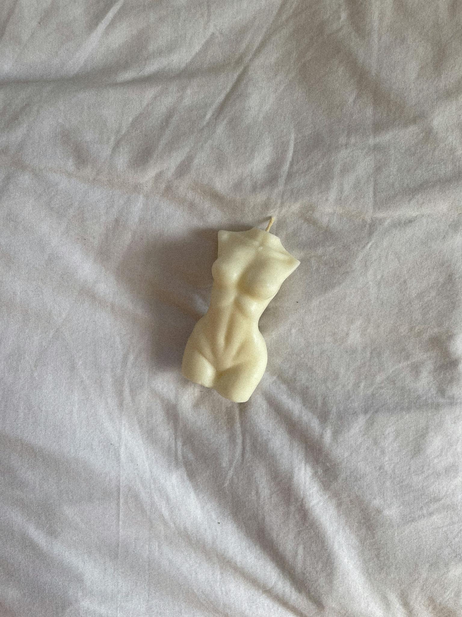 An artistic sculptural candle shaped like a human torso laying on a white sheet.