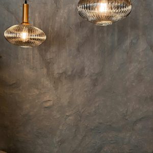 Glowing spherical chandeliers hanging against rough uneven gray wall above chairs in dark room