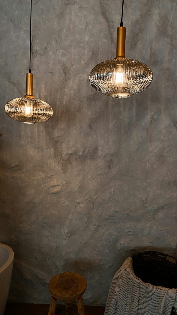 Glowing spherical chandeliers hanging against rough uneven gray wall above chairs in dark room